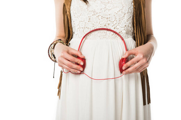 cropped view of pregnant hippie woman holding headphones on belly isolated on white