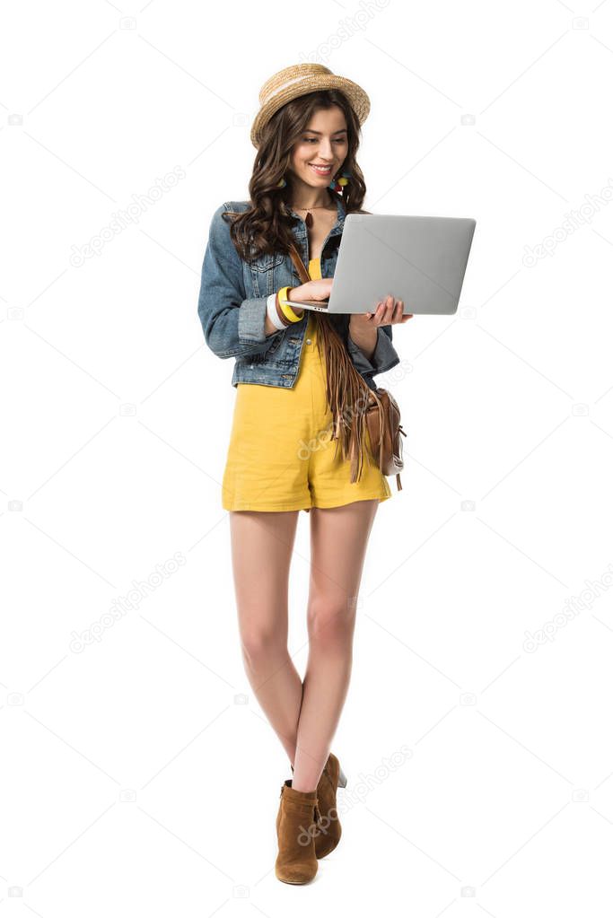 full length view of cheerful boho girl in boater holding laptop isolated on white