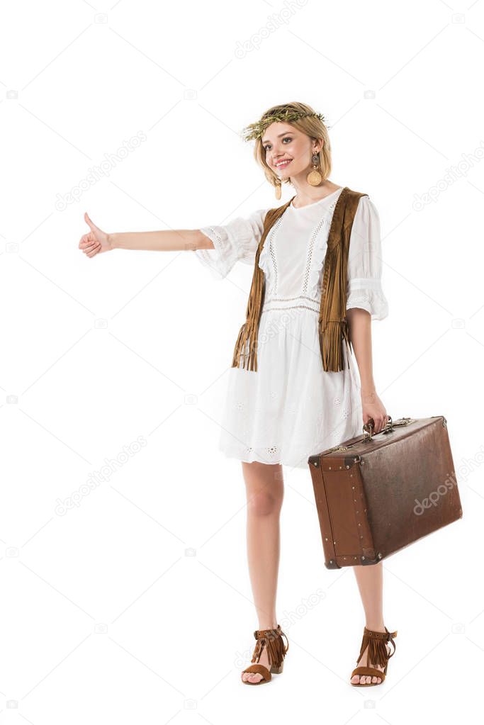 full length view of smiling boho girl holding suitcase and hitchhiking isolated on white