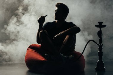 silhouette of man sitting on bean bag chair and smoking hookah clipart