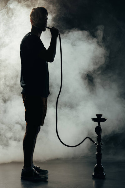 full length view of silhouette smoking hookah in darkness