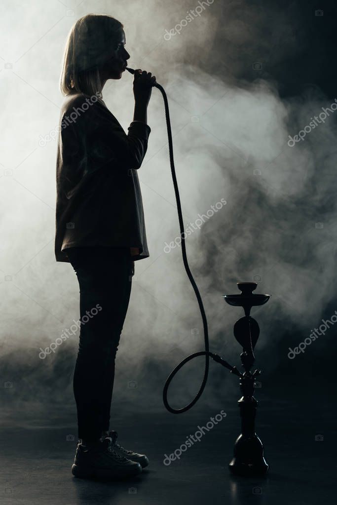 vista lateral de la silueta de la mujer fumar narguile en la oscuridad 2023