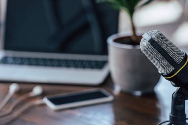 ahşap masada boş ekran ile dizüstü bilgisayar ve akıllı telefon yakınında mikrofon seçici odak