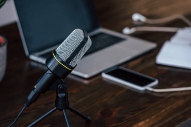 ahşap masada boş ekran ile dizüstü bilgisayar ve akıllı telefon yakınında mikrofon seçici odak