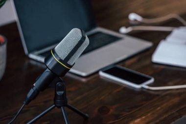 selective focus of microphone near laptop and smartphone with blank screen on wooden table clipart