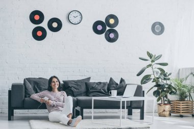 evde yerde otururken kulaklık müzik dinle ve akıllı telefon tutan neşeli kadın
