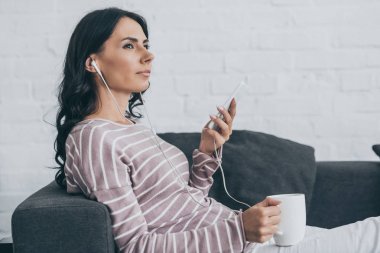 çekici dalgın kadın kulaklık müzik dinleme ve kanepe üzerinde dinlenirken uzağa bakıyor