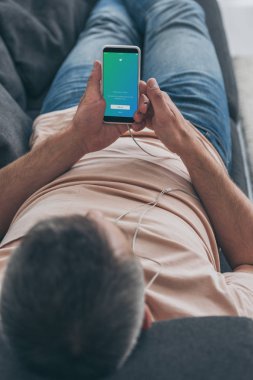 Kiev, Ukrayna - 5 Mayıs 2019: Kanepede yatan ve akıllı telefon ile twitter uygulamasını ekranda tutan adamın seçici odağı.