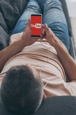 Kiev, Ukrayna - 5 Mayıs 2019: Kanepeye yaslanıp ekranda Youtube uygulaması olan akıllı telefonu tutan insanın seçici odağı.
