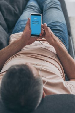 Kiev, Ukrayna - 5 Mayıs 2019: Kulaklıklı adamın kanepede yatan ve ekranda Skype uygulaması olan akıllı telefonu tutan seçici odağı.