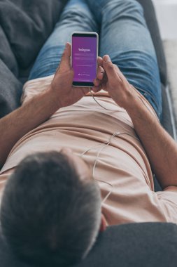 Kiev, Ukrayna - 5 Mayıs 2019: Kulaklıklı adamın kanepede yatan ve ekranda Instagram uygulaması olan akıllı telefonu tutan seçici odak noktası.