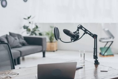 radyo stüdyosunda ahşap masa üzerinde micropohone, dizüstü bilgisayar ve su bardağı