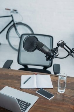 Mikrofon, dizüstü bilgisayar, boş ekranlı akıllı telefon ve yayın stüdyosunda not defteri olan iş yeri