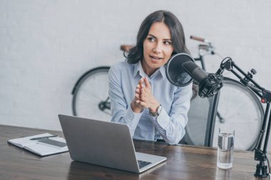 pretty radio host speaking in microphone while sitting at desk near laptop  clipart
