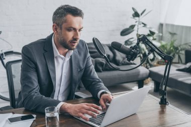 mikrofon yakınında işyerinde otururken dizüstü bilgisayar kullanarak yakışıklı radyo host
