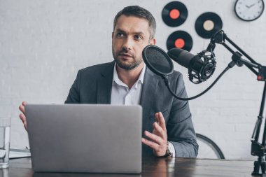 dizüstü bilgisayarın yakınındaki işyerinde mikrofonda konuşurken yakışıklı radyo host gesturing 