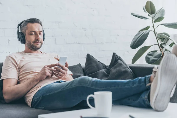 Handsome Man Headphones Using Smartphone While Sitting Sofa Crossed Legs — Stock Photo, Image