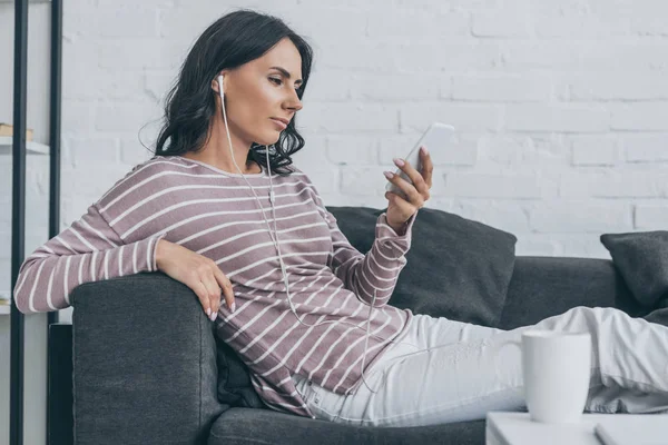 Pensive Woman Sitting Sofa Holding Smartphone Listening Music Earphones — Stock Photo, Image