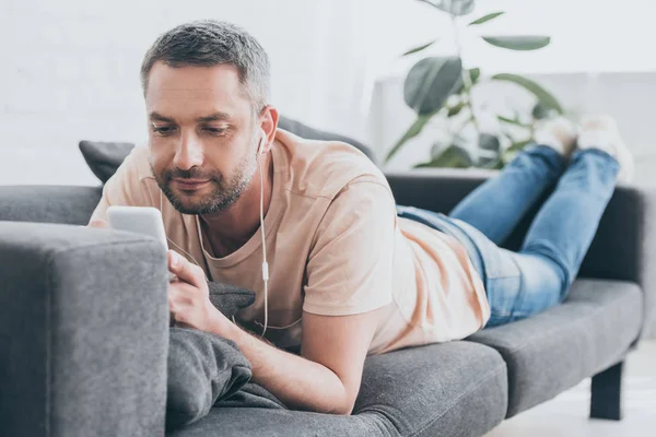 Pria Tersenyum Mendengarkan Musik Earphone Dan Menggunakan Smartphone Sambil Beristirahat — Stok Foto