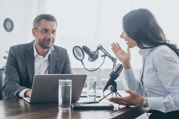 Uśmiechnięty Radio Host Patrząc Businesswoman Wskazując Siedząc Pobliżu Mikrofonu Radio — Zdjęcie stockowe