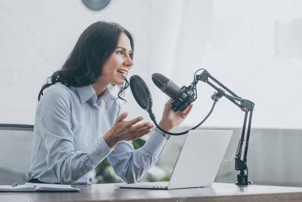 pretty radio host speaking in microphone and gesturing in broadcasting studio