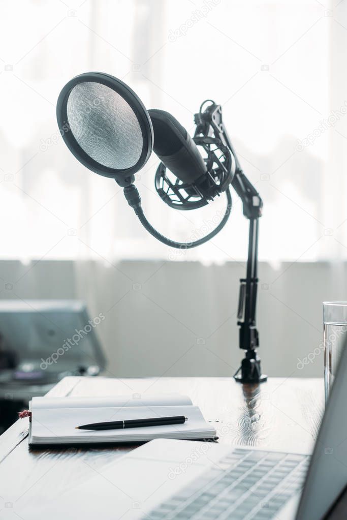 selective focus of microphone fixed on table near laptop in broadcasting studio