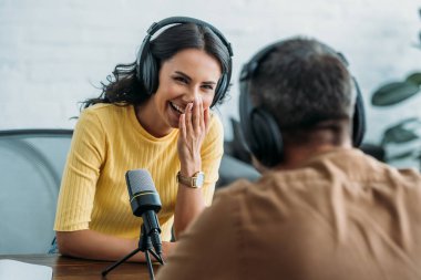 selective focus of cheerful radio host laughing while recording podcast with colleague 