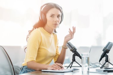 attractive serious radio host in headphones gesturing while looking at camera   clipart