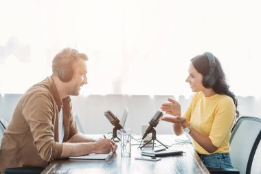 two smiling radio hosts talking while recording podcast in broadcasting studio clipart