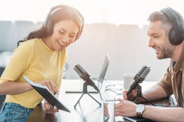 neşeli radyo host gülümseyen meslektaşının yanında otururken dizüstü parmağıile işaret