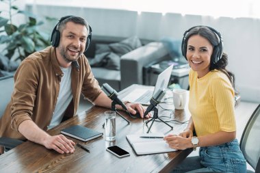yayın stüdyosunda işyerinde otururken kameraya gülümseyen iki neşeli radyo hosts