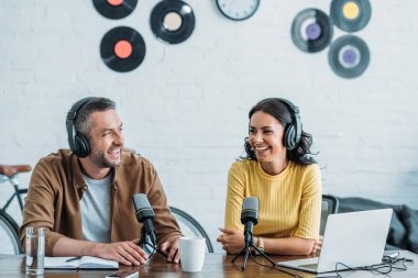 iki neşeli radyo hosts mikrofonlar yanında oturan ve stüdyoda podcast kayıt