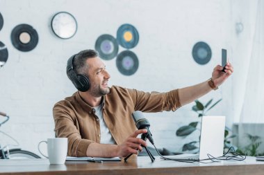 işyerinde otururken akıllı telefon ile selfie çeken kulaklık neşeli radyo host 
