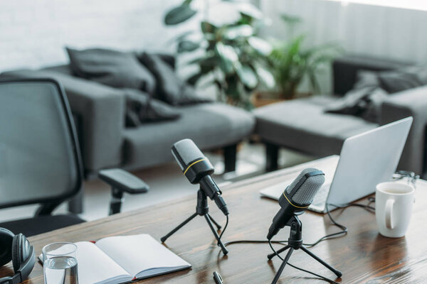 рабочее место с двумя микрофонами, ноутбуком, ноутбуком и кофейной чашкой в студии вещания
