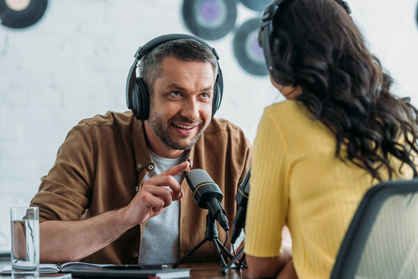 smiling radio host gesturing while talking to colleague in broadcasting studio