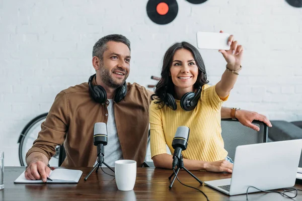 Piękne Radio Host Siedzi Blisko Przystojny Kolega Biorąc Selfie Smartfonem — Zdjęcie stockowe