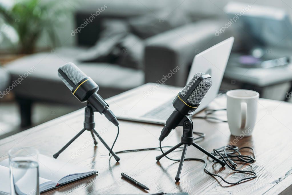 two microphones, laptop, notebook and coffee cup on wooden table in radio studio