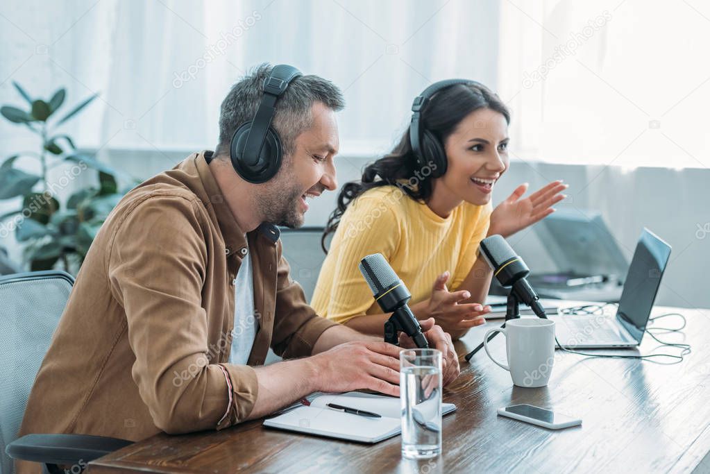 two cheerful radio hosts in headphones recording podcast in studio