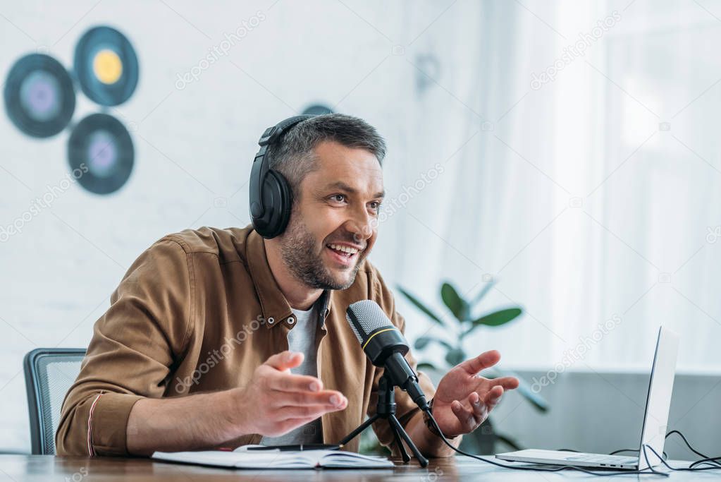 smiling radio host in headphones gesturing while speaking in microphone in broadcasting studio