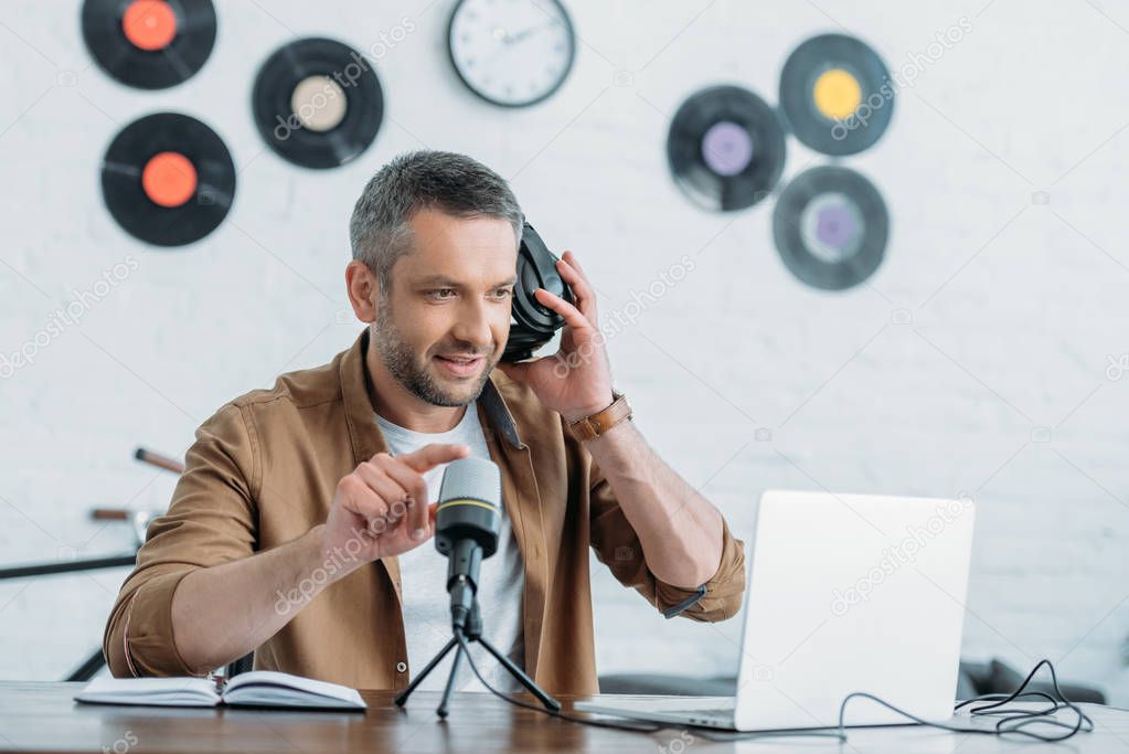 handsome radio host holding adjusting headphones and microphone in broadcasting studio