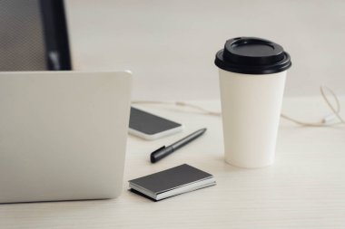 ofis masasında siyah boş kartvizit, tek kullanımlık bardak, dizüstü bilgisayar, akıllı telefon ve kalem yığını
