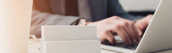 частичный просмотр бизнесмена с помощью ноутбука рядом с держателем карты с пустыми визитными карточками, панорамный снимок
