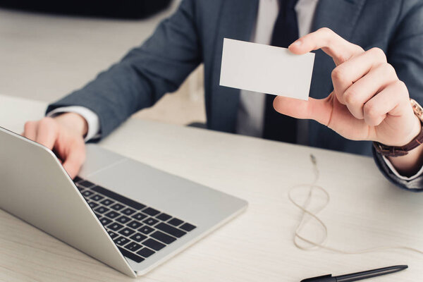 частичный просмотр бизнесмена, показывающего чистую визитную карточку на камеру при использовании ноутбука
