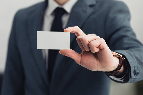 cropped view of businessman in formal wear showing empty business card at camera