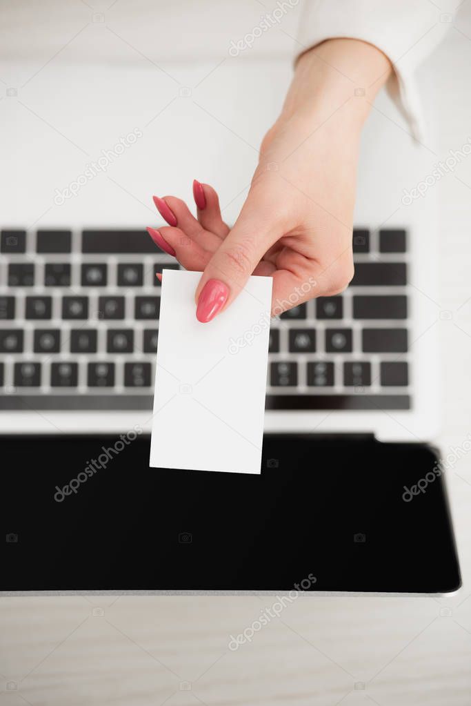 top view of businesswoman holding white blank business card near laptop 