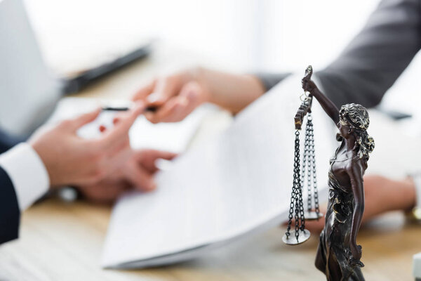 selective focus of themis figurine and businesspeople signing contract 