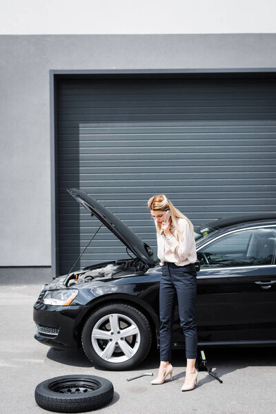 деловая женщина разговаривает на смартфоне рядом со сломанным автомобилем, концепция страхования автомобиля
