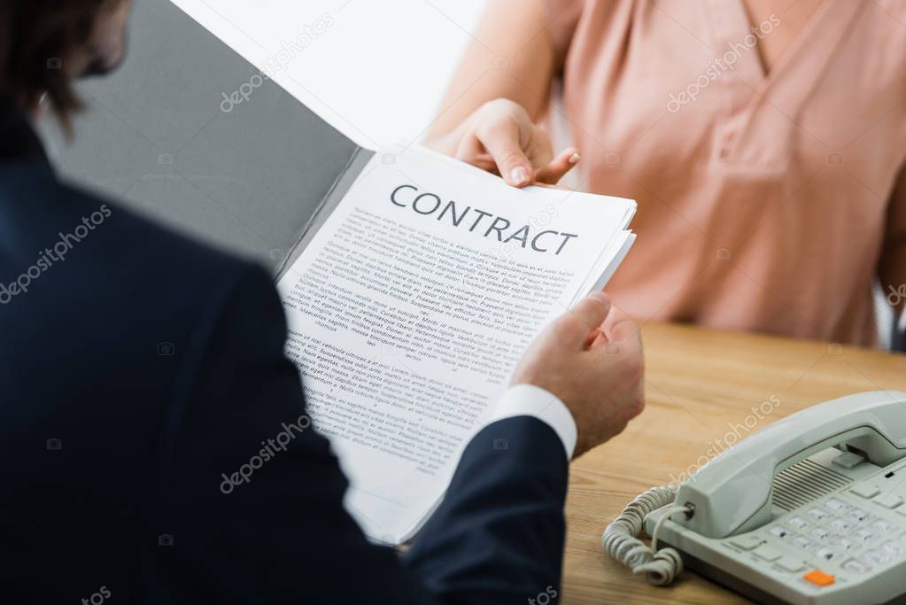 cropped view of woman and businessman holding contract in hands