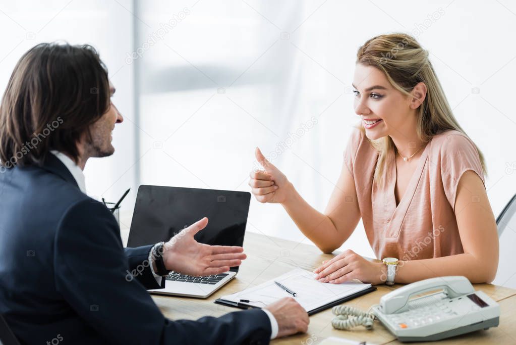 cheerful woman looking at businessman and showing thumb up sign