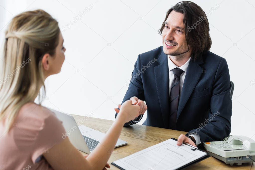 selective focus of happy businessman holding contract in hand and shaking hands with client